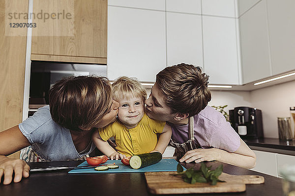 Happy lesbian couple kissing their child in kitchen