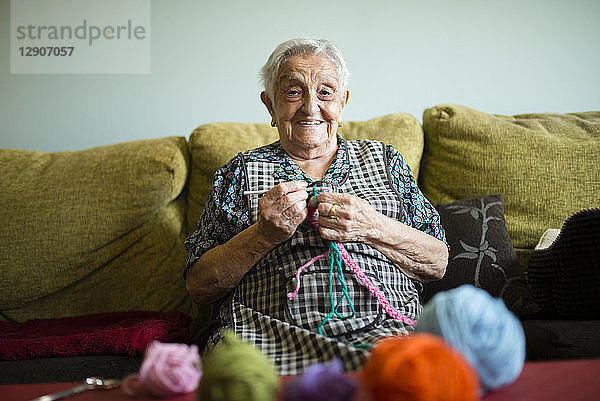 Portrait of smiling senior woman crocheting on the couch at home