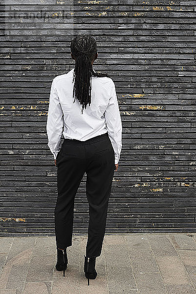 Back view of businesswoman with dreadlocks wearing white shirt and black trousers
