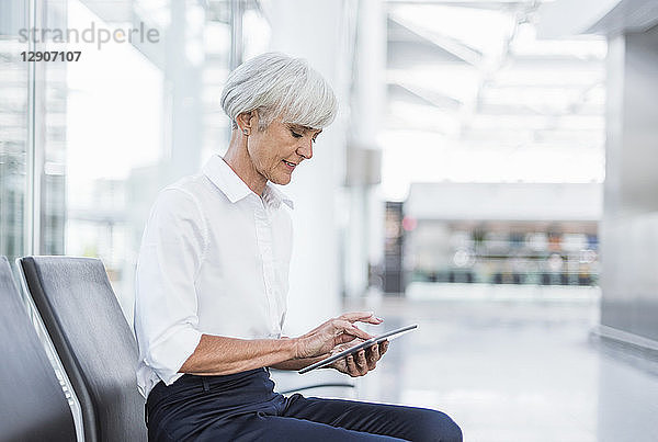 Senior businesswoman sitting in waiting area using tablet
