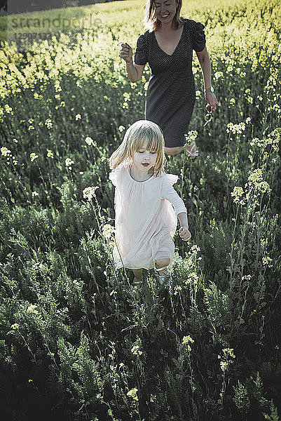 Portrait of little girl walking on rape field with her mother