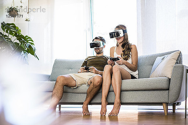 Couple sitting on couch at home wearing VR glasses playing video game