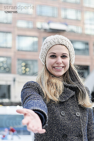 Pretty blond young woman wearing wool cap in winter  reaching out hand