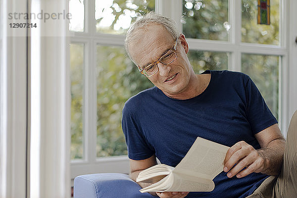 Smiling mature man at home reading book
