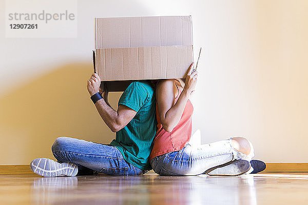 Couple with heads in cardboard box sitting back to back on the floor at new home