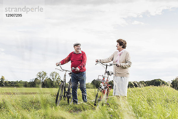 Senior couple pushing bicycles in rural landscape