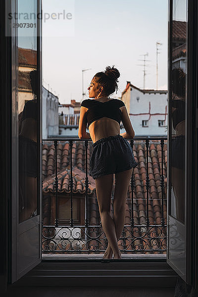 Beautiful young woman standing on balcony at sunset
