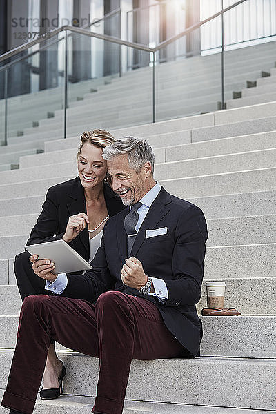 Two business people sitting together on stairs looking at tablet