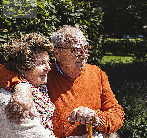 Senior couple sitting on bench in a park  with arms around