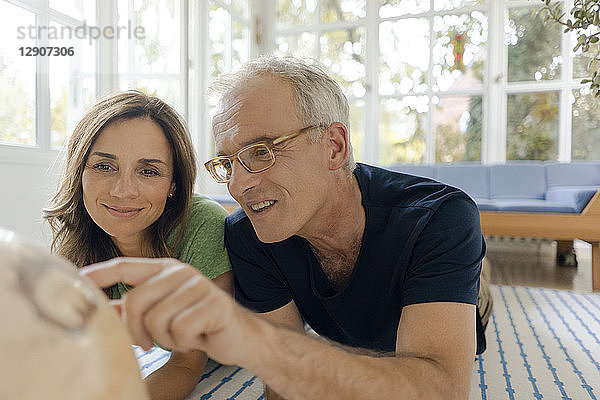 Mature couple lying on the floor at home looking at globe
