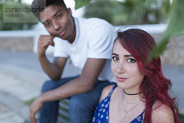 Portrait of young woman with dyed red hair sitting on bench with her boyfriend