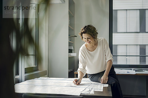 Businesswoman sitting in office  working on blueprints