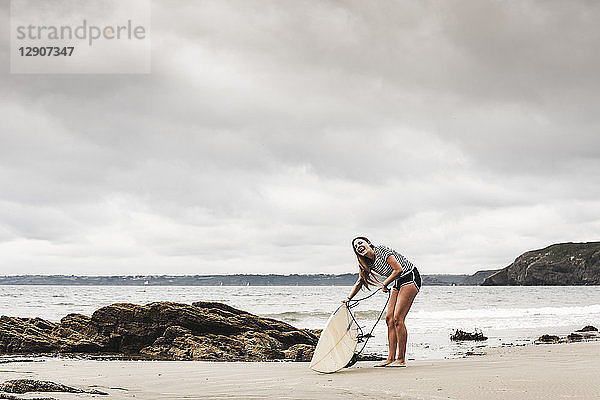 Young woman at the beach preparing surfboard