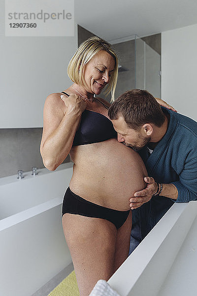 Mature husband kissing expectant mother?s belly in bathroom