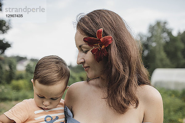 Mother with flower in her hair holding baby in garden