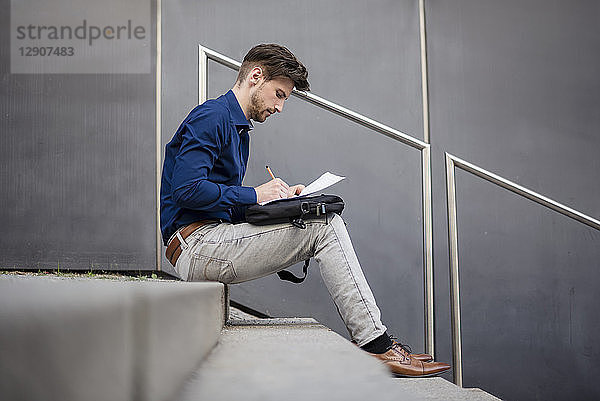 Businessman sitting on stairs outdoors taking notes