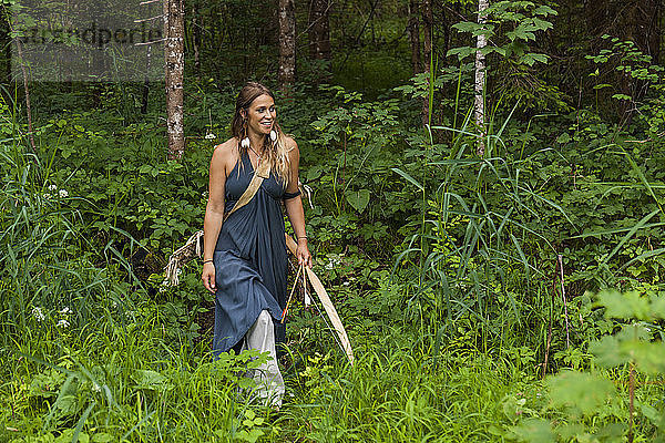 Smiling woman walking in a forest with bow and arrow