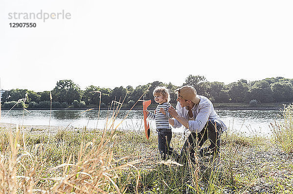 Father and son having fun at the riverside  playing with toy aeroplane