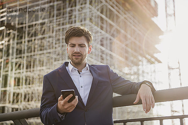 Businessman standing on bridge in front of construction site using cell phone