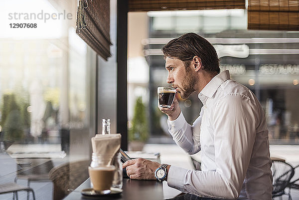 Businessman with tablet in a cafe drinking coffee from glass