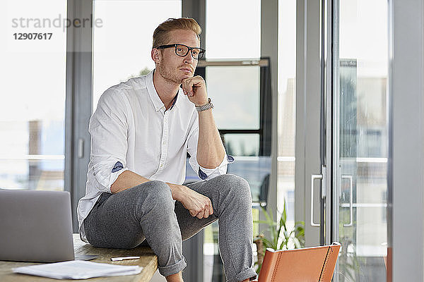 Serious businessman with laptop sitting on desk in office