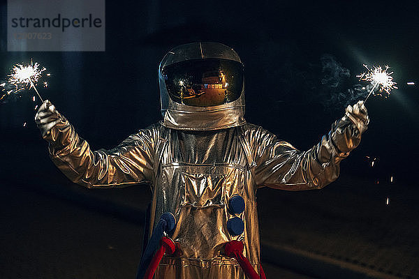Spaceman standing on a road at night holding sparklers