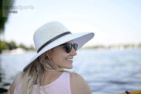 Smiling young woman wearing sunglasses and white summer hat al lake