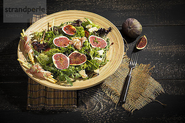 Mixed salad with figs  tomatoes  sheep cheese  grissini with ham on bambus plate