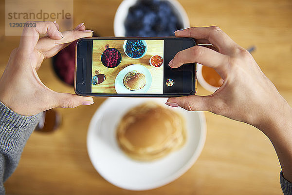 Young woman taking pictures of breakfast pancakes with berries and fresh fruit