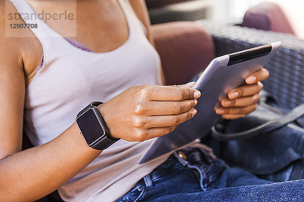 Young woman with smartwatch sitting at sidewalk cafe using digital tablet  close-up