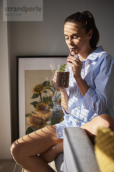 Young woman drinking smoothie at home