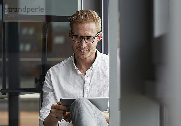 Smiling businessman sitting on windowsill using tablet