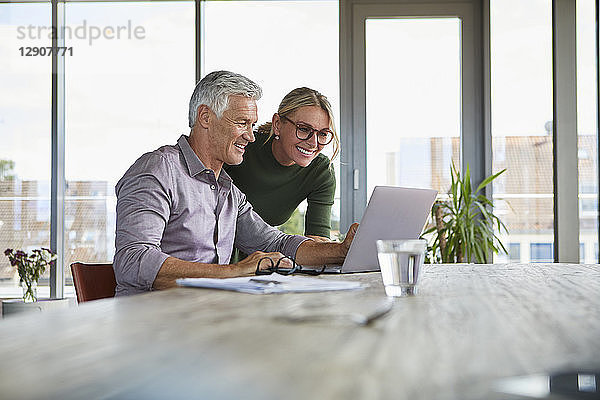 Smiling mature couple using laptop on table at home