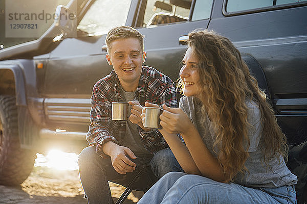 Young couple sitting by car  taking a break  drinking tea