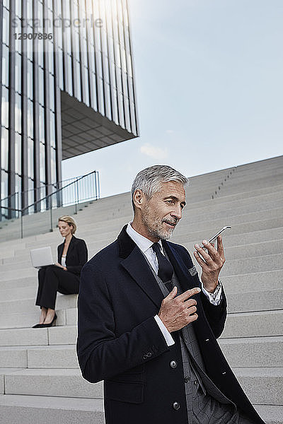 Portrait of businessman talking on the phone while business woman working on laptop in the background