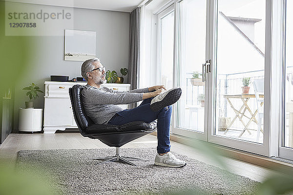Mature man relaxing on leather chair in his living room looking out of window