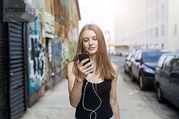 Young woman walking in street  listening music  using smartphone