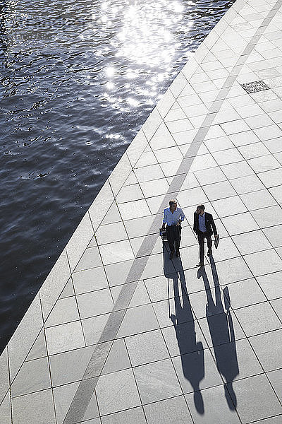 Two businessmen walking and talking at the riverbank