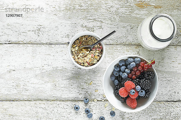 Bowl of granola  milk bottle and bowl of berries on wood