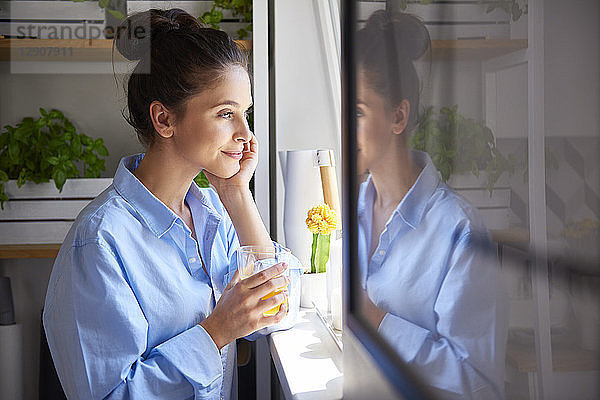 Young woman drinking orange juice in her kitchen
