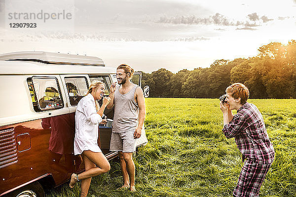 Woman taking picture of friends brushing teeth at a van in rural landscape