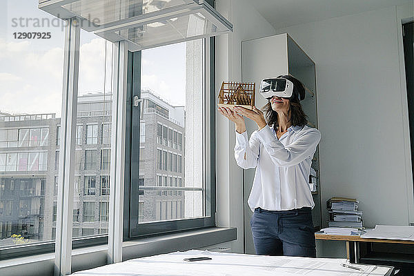 Woman holding architectural model of house  using VR glasses
