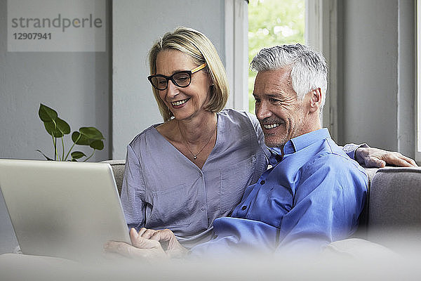 Happy mature couple sitting on couch at home sharing laptop