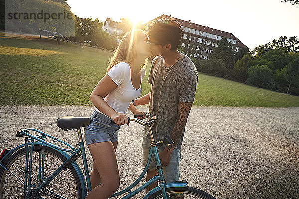 Young woman with bicycle  kissing her boyfriend in park