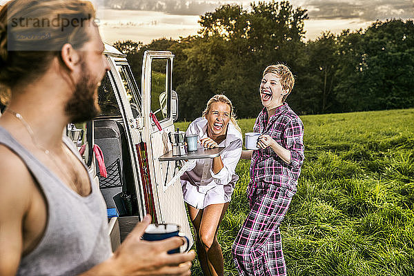 Carefree friends enjoying coffee at a van in rural landscape