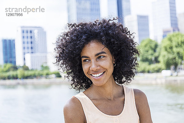 Germany  Frankfurt  portrait of smiling young woman with curly hair in front of Main River