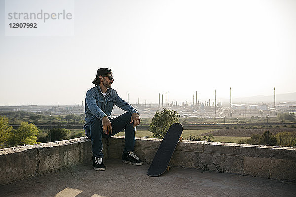 Skateboarder dressed in casual clothes resting at sunset