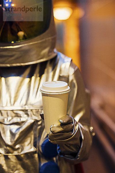 Spaceman in the city at night holding takeaway coffee