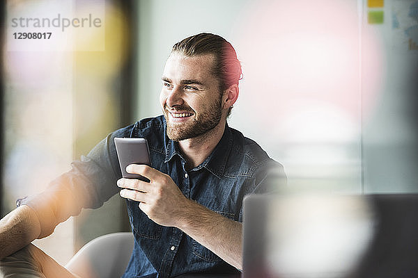 Smiling young businessman in office holding cell phone