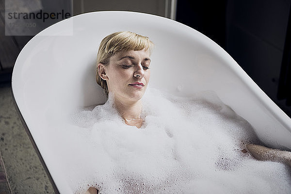 Portrait of woman with eyes closed taking bubble bath in a loft